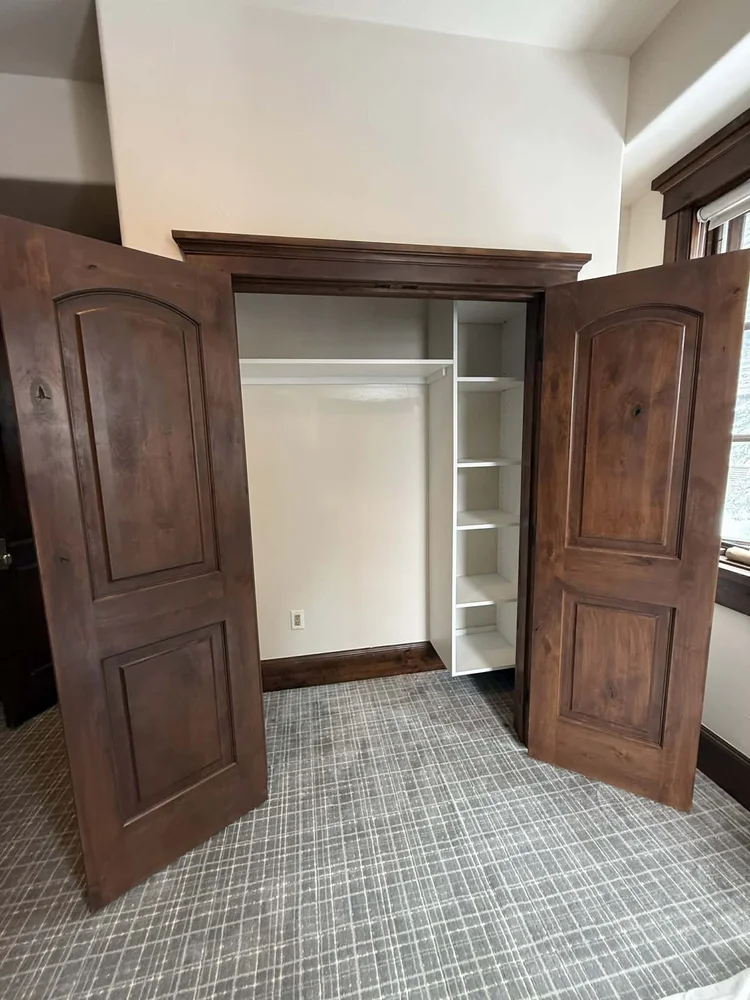 Finished bedroom closet with white shelving behind arched alder doors
