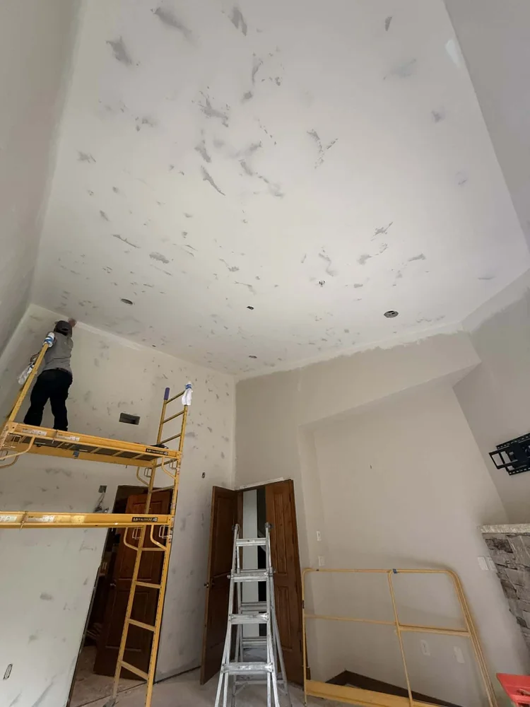 Skim coat being applied to a high ceiling during an interior remodel