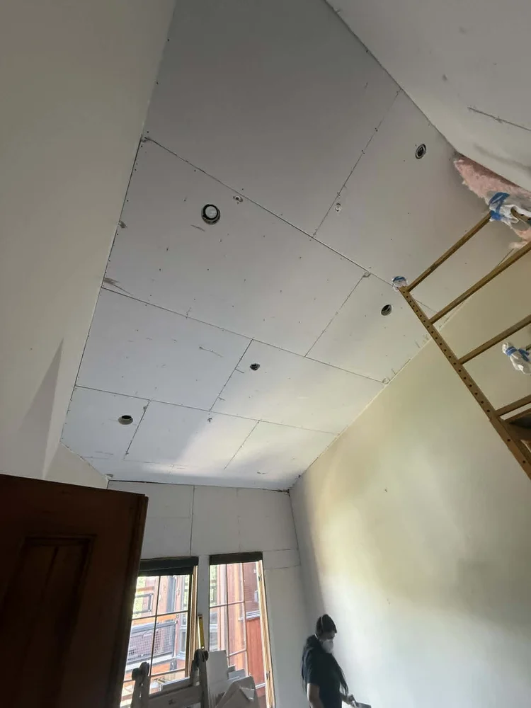 Drywall being installed on a vaulted ceiling during an interior remodel