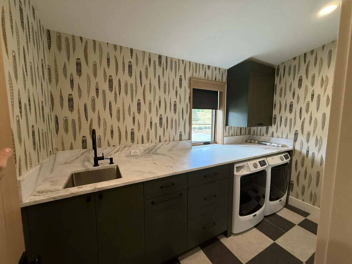Finished laundry room with marble countertop, dark green cabinetry and patterned wallpaper